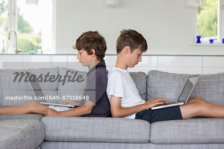 Brothers back to back on sofa using computers