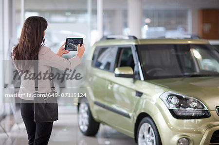 Mid adult woman taking photograph of car in showroom