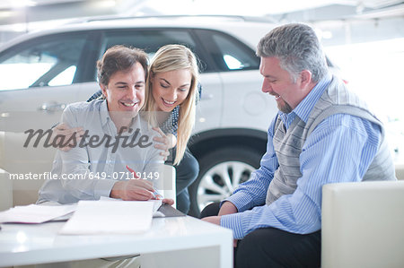 Car salesman and couple signing contract in car showroom