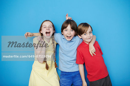 Portrait of three children with arms around each other against blue background