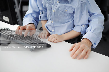Boy sitting on father's lap using computer keyboard