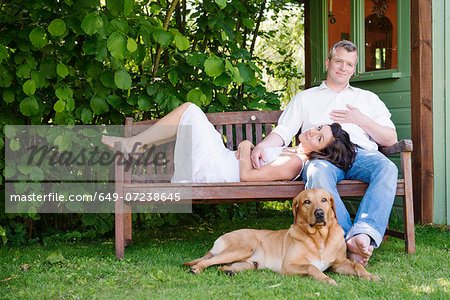 Portrait of mature couple on garden bench with dog