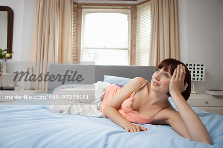 Young woman lying on bed daydreaming