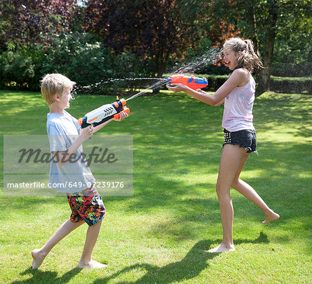 Brother and sister play fighting with water guns in garden Brother and sister play fighting with water guns in garden