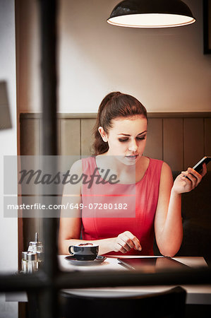 Young woman sitting in cafe with hot drink, digital tablet and smartphone