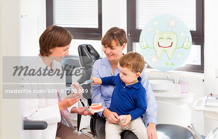 Dentist teaching boy on mothers lap how to brush teeth