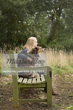 Teenage girl sitting on country bench with dog