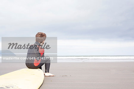 Boy sitting on surfboard on beach