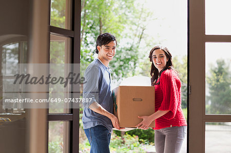 Young couple carrying cardboard box into new house