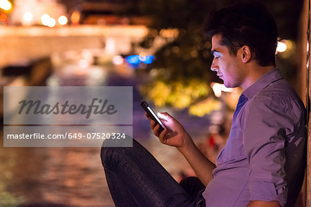 Young man looking at smartphone at night, Paris, France