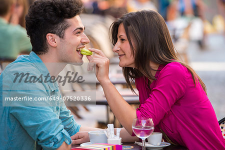 Young couple eating macaroon at pavement cafe, Paris, France