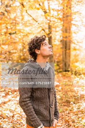 Portrait of man wearing cardigan in forest looking up