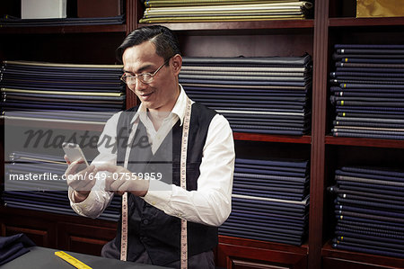 Tailor texting on cellphone in tailors shop