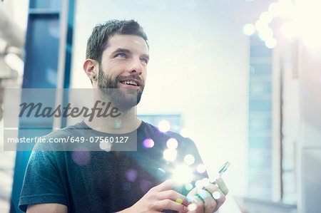 Mid adult man looking up at lights coming from smartphone Mid adult man looking up at lights coming from smartphone