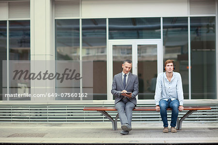 Businessman and young man sitting on train station bench