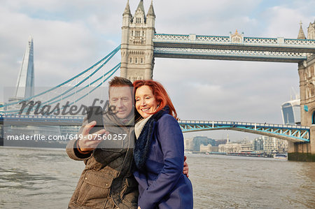 Mature tourist couple photographing selves and Tower Bridge, London, UK