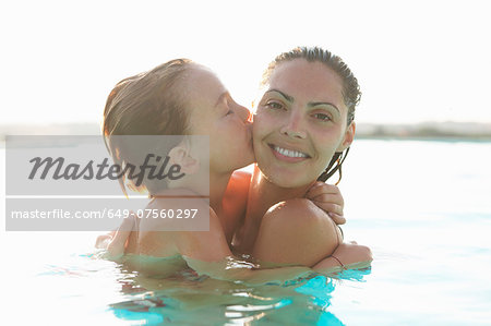 Portrait of mother and son in outdoor swimming pool, son kissing mother