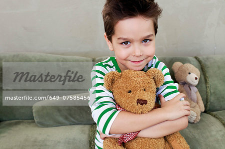 Portrait of young boy on sofa hugging teddy