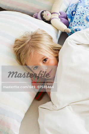 Portrait of young girl lying in bed with doll