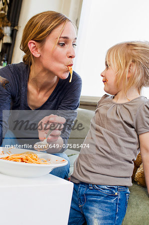 Mid adult mother eating spaghetti with her daughter