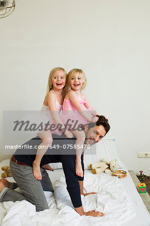 Portrait of mid adult father giving two young daughters a piggy back