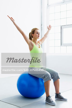 Young woman sitting on exercise ball, arms raised