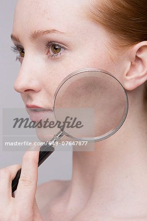Portrait of young woman, magnifying glass on cheek