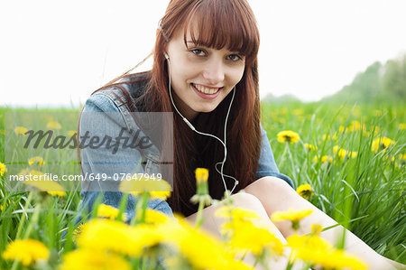 Portrait of young woman in earphones in dandelion field