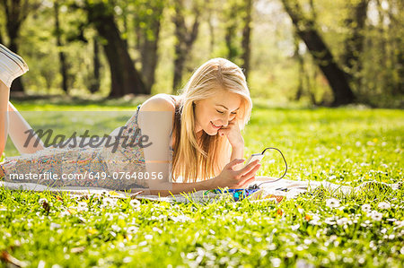 Young woman lying in forest looking at smartphone