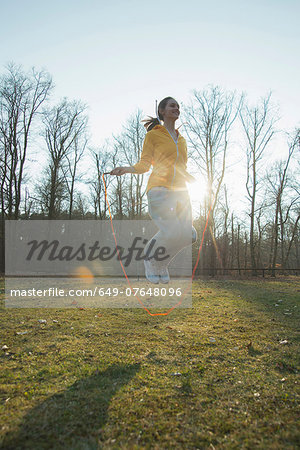 Young woman exercising in field with skipping ropes