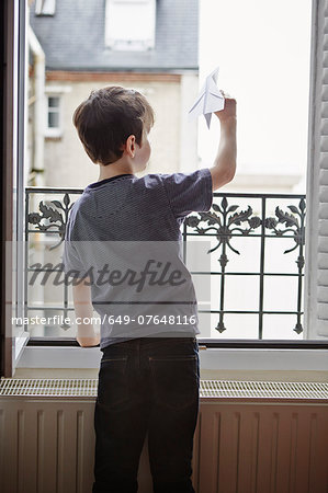 Boy launching paper plane from window
