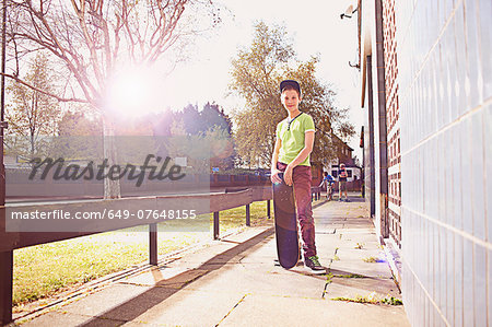 Portrait of boy standing on pavement holding skateboard
