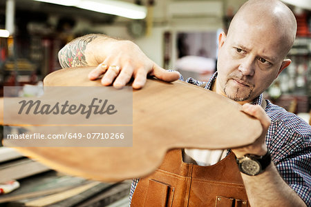 Guitar maker checking wooden guitar shape in workshop