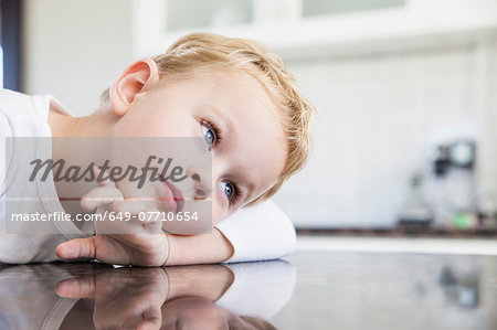 Portrait of three year old boy leaning on kitchen bench