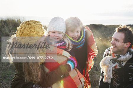 Mid adult couple in sand dunes with their son and daughter wrapped in blanket
