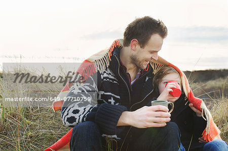 Smiling mid adult man and son wrapped in blanket on sand dunes Smiling mid adult man and son wrapped in blanket on sand dunes