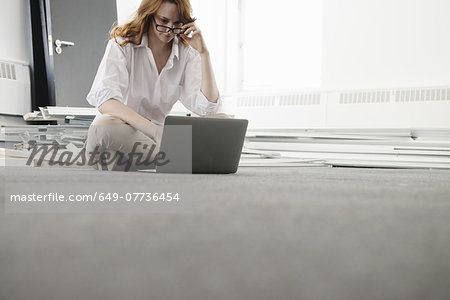 Mid adult businesswoman using laptop on floor in new office