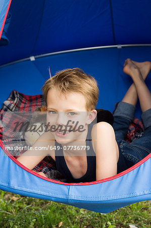 Portrait of smiling boy lying in tent suspended above grass