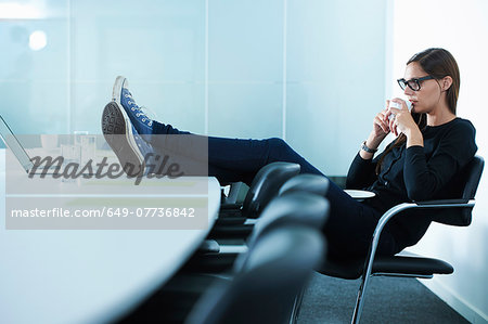 Female office worker drinking coffee with feet up on conference table