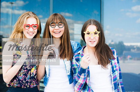 Portrait of three young women holding up spectacle costume masks