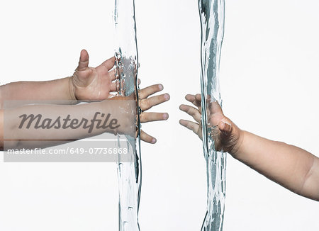 Composite view of toddlers arms and hands reaching out from opposite sides into clear water Composite view of toddlers arms and hands reaching out from opposite sides into clear water