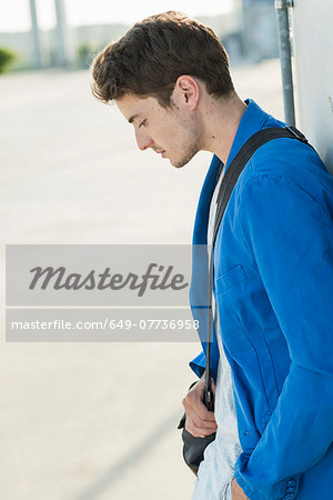 Serious young man with shoulder bag leaning against wall