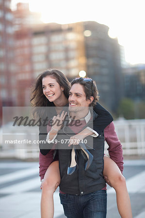 Mid adult man giving girlfriend piggyback in street