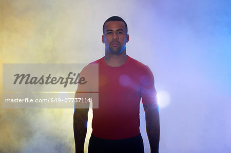 Studio portrait of muscular young sportsman in spotlights and mist