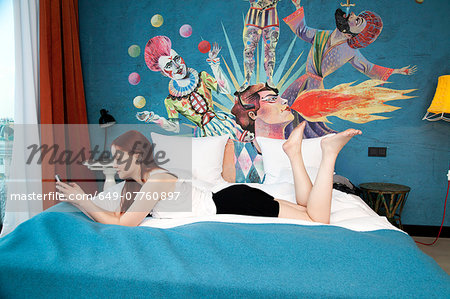 Young woman lying on hotel bed texting on smartphone