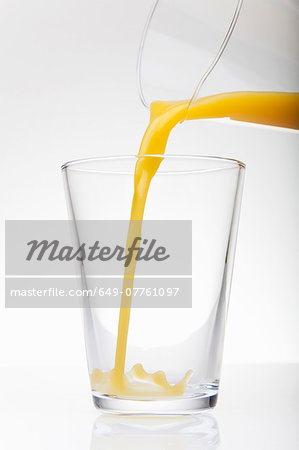 Fresh orange juice pouring from jug into drinking glass