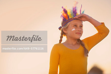 Girl dressed as native american in feather headdress with hand shading eyes