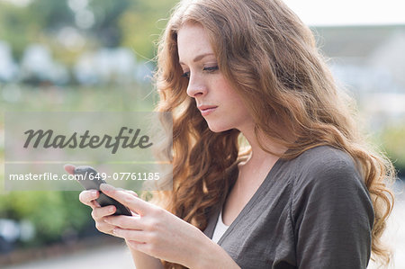 Sullen young woman reading texts on smartphone in garden