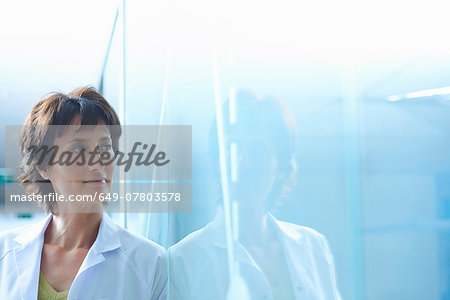 Confident mature businesswoman leaning against glass wall in office