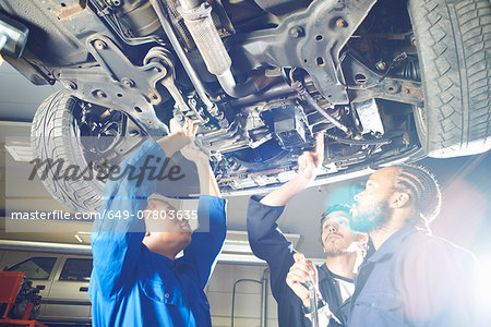 Three college students looking up at car in garage workshop